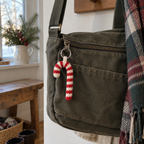 Red and off-white crochet candy cane charm attached by a silver ring to the zipper pull of an olive canvas bag in a home entryway.
