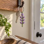 Purple crochet lavender sprig keychain hanging beside a silver house key from a hook on a wooden key rail near the front door.