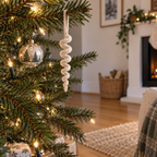 An off-white crochet icicle spiral hanging by its yarn loop on a green Christmas tree with small warm-white lights.