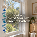 A white cloud crochet wind spinner with a white-edged blue spiral and blue and teal raindrops hangs in a bright nursery window beside the title Rain Cloud Wind Spinner Crochet Pattern.