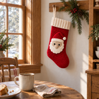 Red crochet Santa stocking hanging by its ivory yarn loop from a wooden peg beside a dining-nook window and breakfast table.