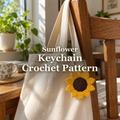 Golden-yellow crochet sunflower keychain with a dark-brown centre hanging from a canvas tote strap in sunlight, with the title Sunflower Keychain Crochet Pattern.