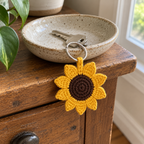 Golden-yellow crochet sunflower keychain attached to house keys in a speckled ceramic dish, hanging over the edge of a wooden cabinet.
