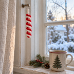 Red-and-white crocheted peppermint spiral ornament hanging from a small peg on a wooden window frame beside a Christmas mug and fir sprig.
