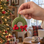An adult hand holding a small green crochet wreath with red berries and a red bow by its green hanging loop.