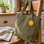 Yellow crochet sun with open loop rays hanging from an olive canvas lunch tote on a kitchen chair.