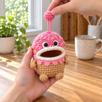 The same adult holds the Donut pouch with an empty mouth while lifting its pink crown ball on two pink chain strands.