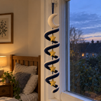 A navy crochet wind spinner with a cream crescent moon and gold stars hangs by a bedroom window at dusk beside warm lamplight.