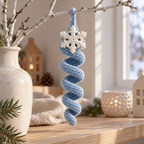 An ice-blue crochet spiral with an ivory snowflake hanging from a white-painted branch in a vase on a wooden shelf