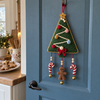 Green tree crochet door hanger with gold star, cream zigzag garland, red trunk bow, candy cane charms and a brown gingerbread charm on a pantry door.