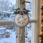 White and ice-blue crochet bauble door hanger with a silver and white snowflake, crocheted pinecones and three charm dangles on a frosty window latch.