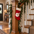 A red Santa crochet stocking hanging from a staircase banister decorated with evergreen garland.