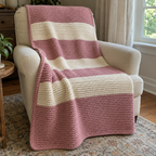 Dusty pink and cream ridged crochet throw with a pink border draped over a cream armchair beside a window.