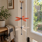 A Twin Rotor with rust-orange upper blades, sand-coloured lower blades and a slate-grey cord hangs from a wooden peg beside a glazed back door.