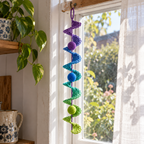 A purple, blue and green lace crochet spinner with three matching balls hanging beside a sheer window curtain