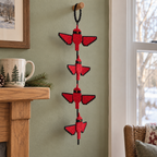 A red Cardinal crochet wind spinner with black-edged wings hangs from a wooden peg beside a window and a mantel with a winter mug.
