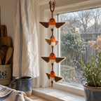 An orange-breasted Robin crochet wind spinner with brown wings and cream bellies hangs at a kitchen window beside a blue mug and rosemary plant.