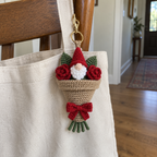Gnome and red rose crochet bouquet with a kraft wrapper and red bow clipped to a canvas tote.