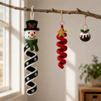 A crochet snowman spiral spinner, a red star spiral ornament and a Christmas pudding charm hanging securely from a bare indoor branch