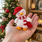 A small white crochet duck with a red cap, striped scarf and Christmas stocking held in an adult palm.