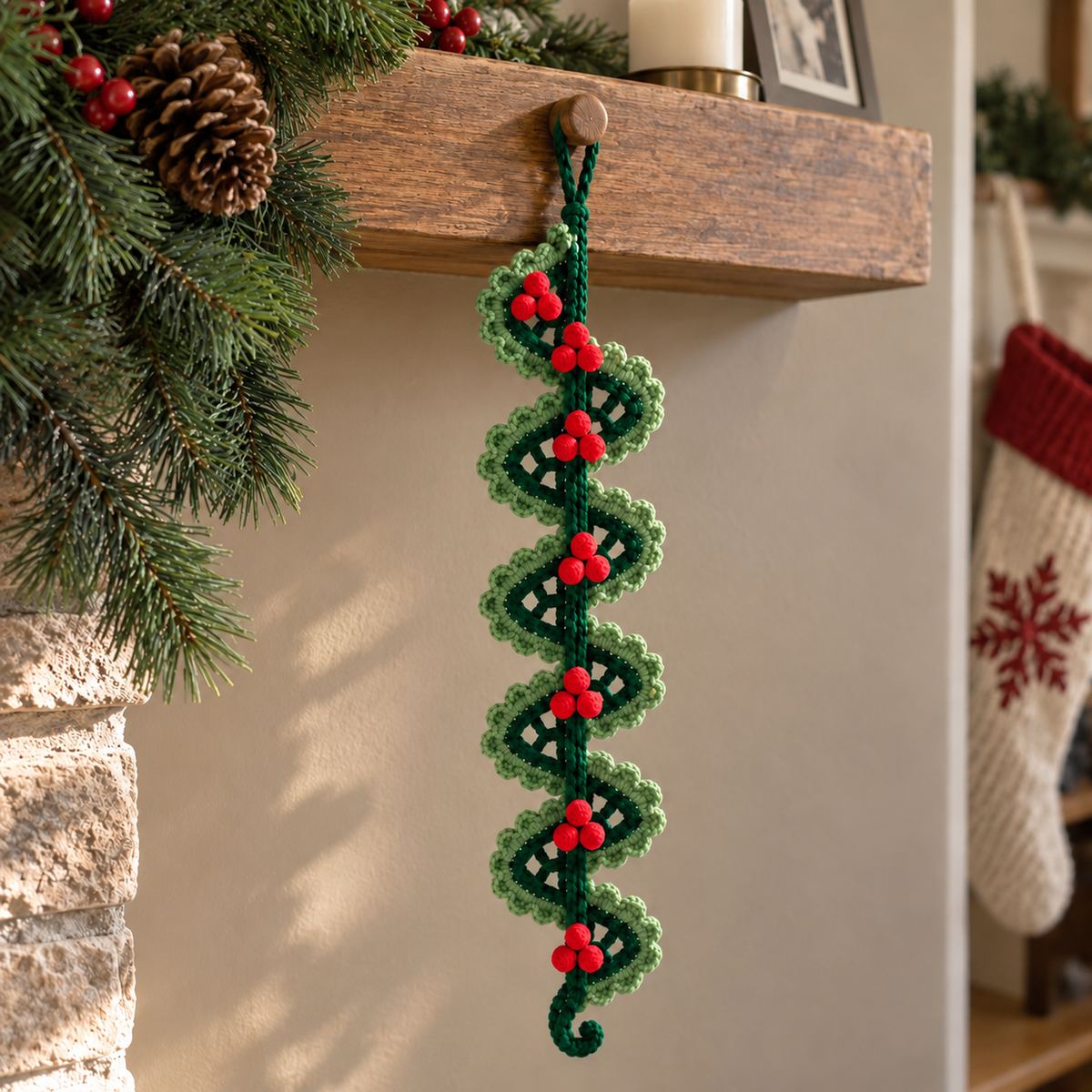 A forest-green crochet lace spiral with sage shell edging and red crochet berry clusters hanging from a wooden mantel peg.