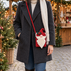 Red gnome crochet phone bag with a pink nose, white loop beard and holly hat worn crossbody over a charcoal winter coat at a Christmas market.