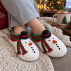 Crossed ankles wearing white Snowman slippers with carrot noses and striped scarf tails on a knitted sofa throw.