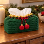 Forest-green crochet tissue box cover with gold lace, a red bow and two red baubles with gold caps on a Christmas entry console.