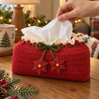 An adult hand pulls a white tissue from a red crochet cover, showing cream lace, green cord through red eyelets and two pointed flower ornaments.