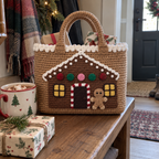 A caramel crochet tote with a gingerbread house front rests on a hallway bench beside cocoa and wrapped gifts, with small gifts peeking above its snowy rim.