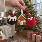 An adult hand holding the Christmas pudding, gingerbread house and red hot cocoa crochet ornaments by their yarn loops in front of a Christmas tree.