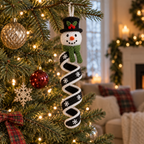 A snowman crochet wind spinner with a green scarf and black spiral hanging from a decorated Christmas tree branch