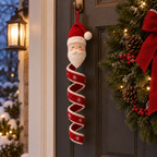 A Santa crochet wind spinner with a red and white spiral hanging on a front door beside an evergreen wreath